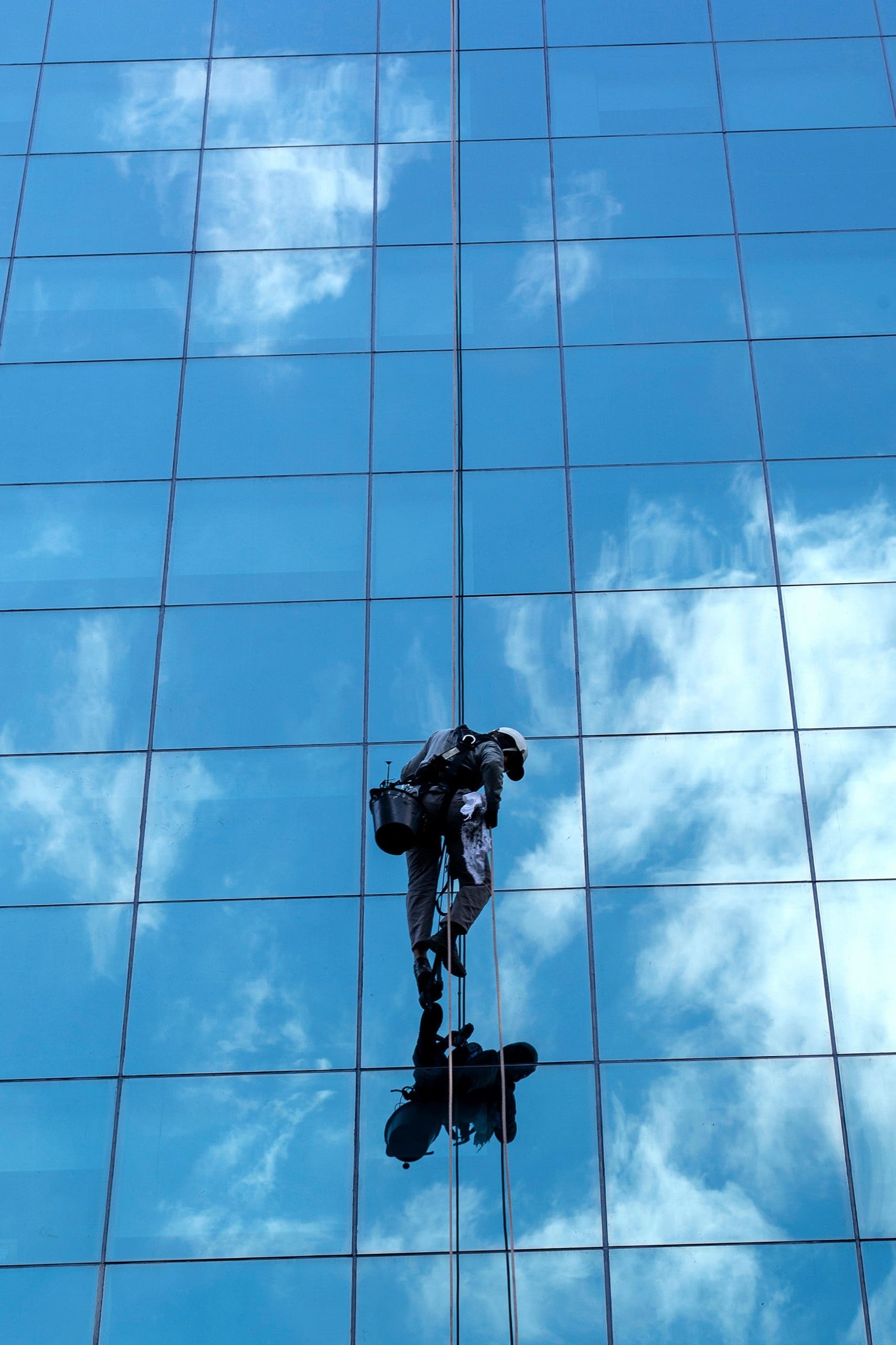 A worker cleaning mirrored windows with a reflection of the sky and clouds of a commercial building in São Paulo, Brazil.