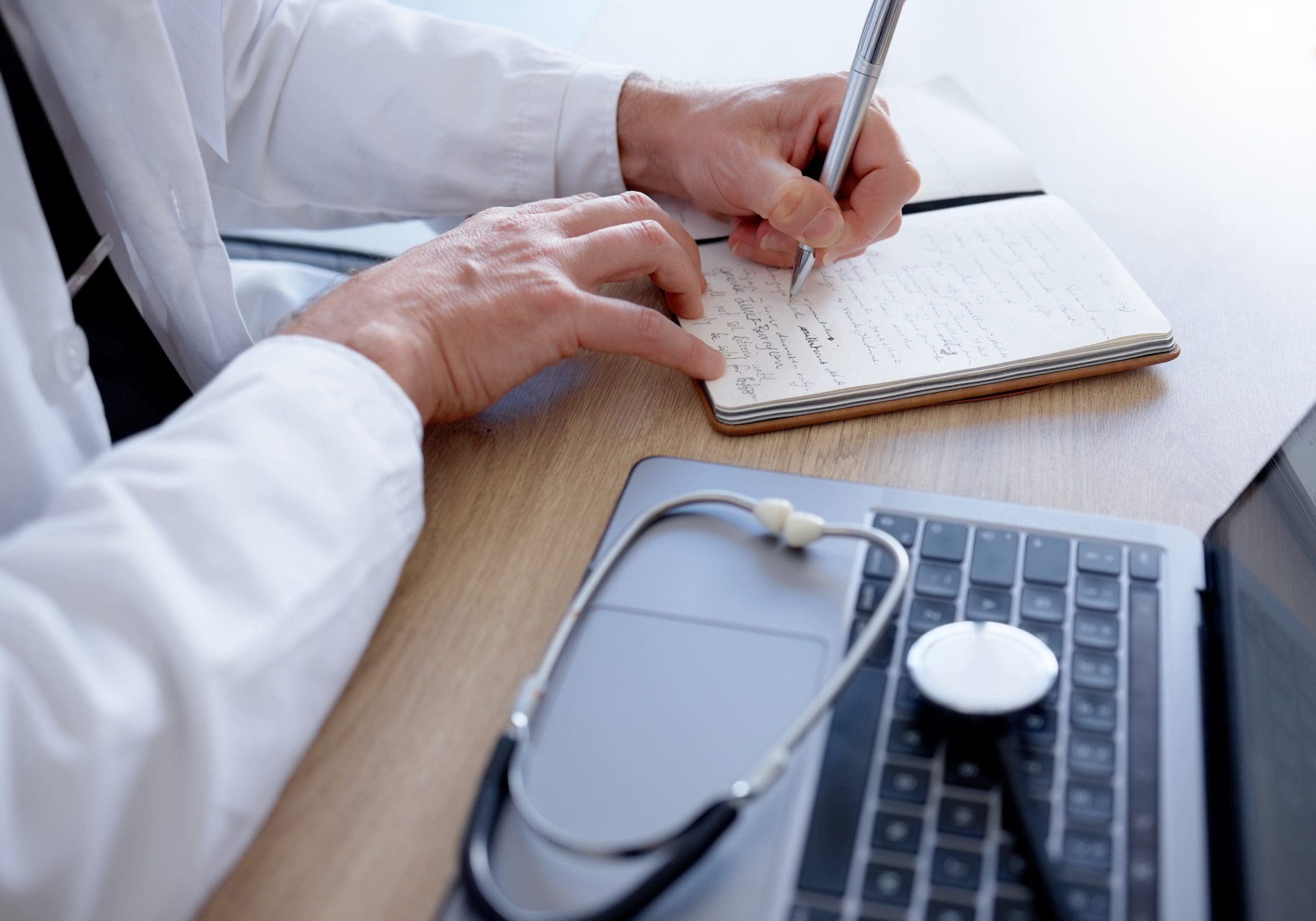 Doctor, writing or hands and notebook, laptop or stethoscope in medical research, ideas or vision in treatment. Zoom, man or healthcare worker and technology, prescription planning or hospital review.